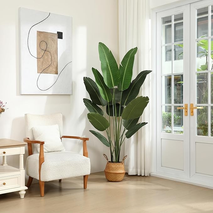 A light beige room with a large potted plant, a cream armchair, and a piece of abstract art on the wall.