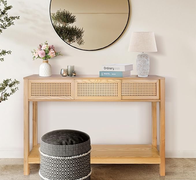 Light wooden console table with cane-style drawers, a round mirror, a lamp, and a decorative stool.