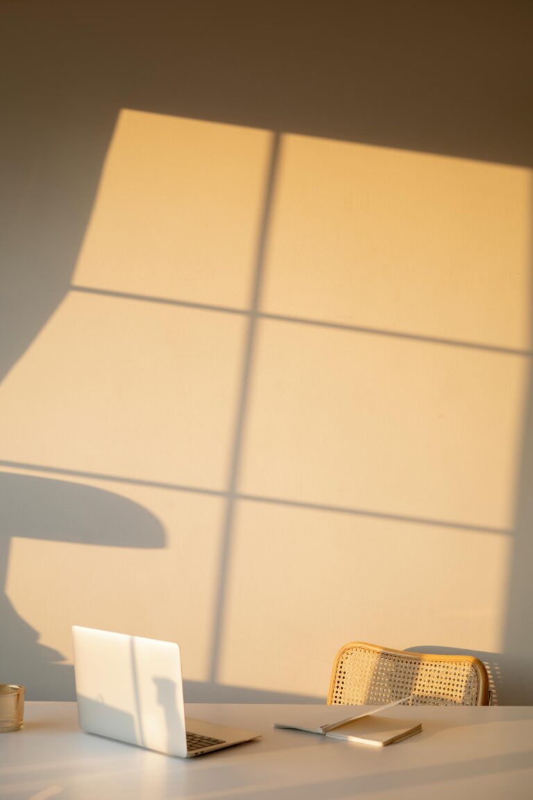 A serene minimalist workspace with natural light casting shadows on a wall, featuring a laptop.