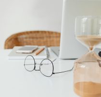 A clean and modern workspace featuring an hourglass and eyeglasses on a desk.