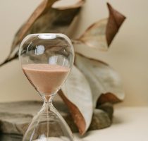 A still life photo of an hourglass with sand, set against dried leaves, symbolizing the passage of time. "productos para organización de escritorio desde Amazon"